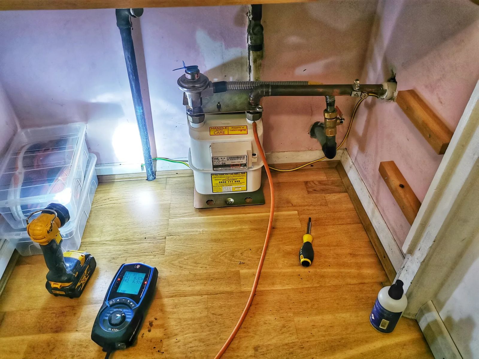 Digital gas pressure gauge on the floor beside a gas meter during a tightness test