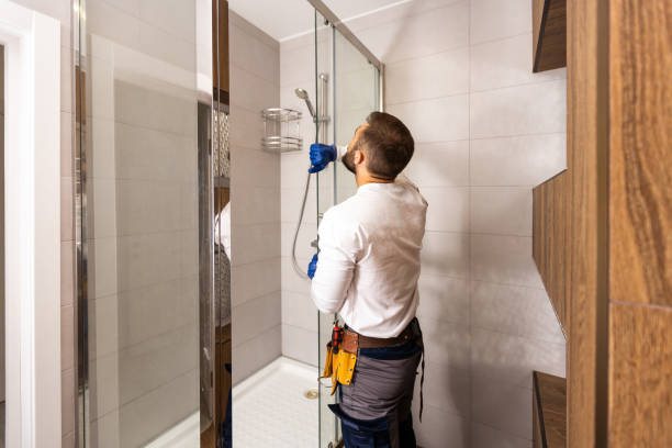 Plumber checking a shower fitting inside a glass shower enclosure