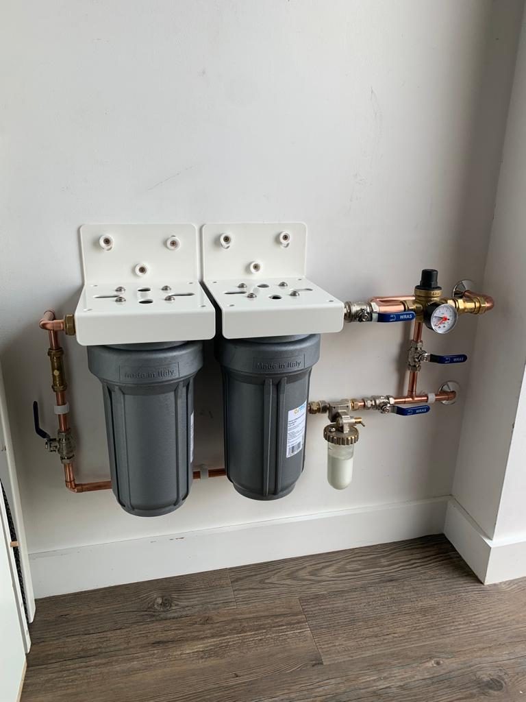 Twin whole-house water filter housings with a pressure reducing valve and gauge